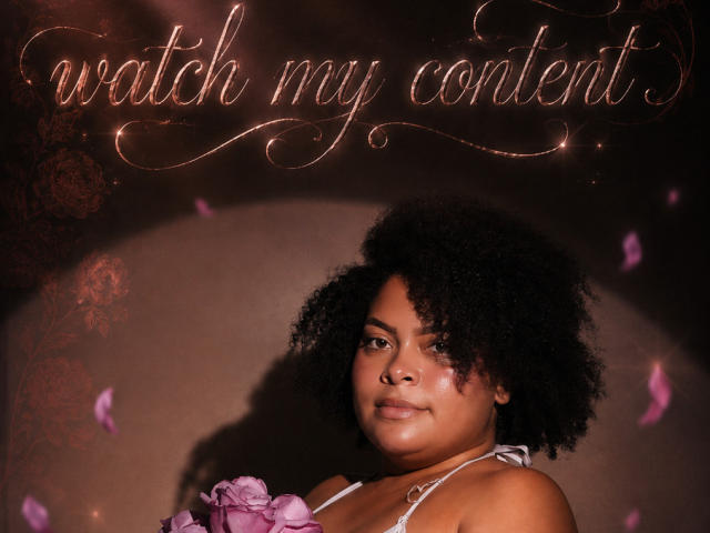 ElizabethBloom has a curvy, brown-skinned face with a big afro, wearing a purple flowered top, showing her tits slightly, with pink petals falling around her.