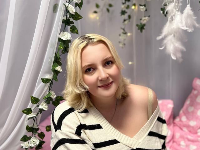 VictoriaNotti with blonde hair, wearing an off-shoulder black and white striped sweater, smiling, and showing her shoulder and a hint of her bra strap.