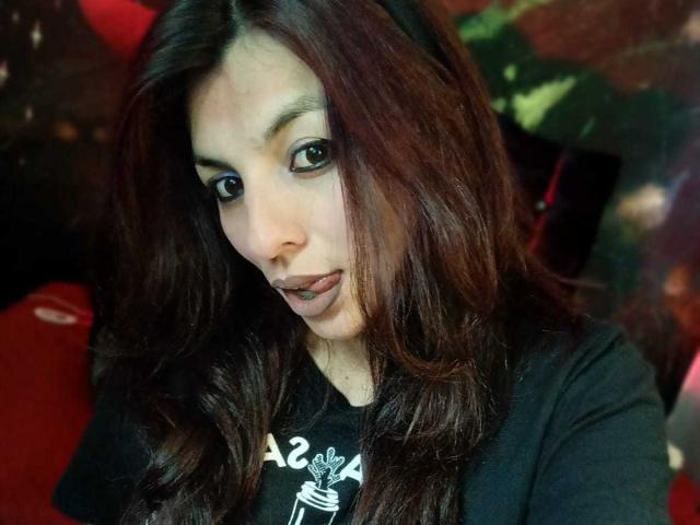 SoyVeronica has wavy dark brown hair, light skin, and is wearing a black shirt. She's looking at the camera with slightly parted lips, brown eyes, and a subtle smile.