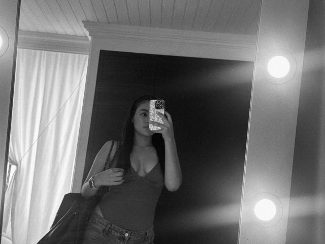 Black-and-white mirror selfie of MiiaPalmer with long dark hair, wearing a low-cut tank top showing her tits, holding a phone, and carrying a bag.