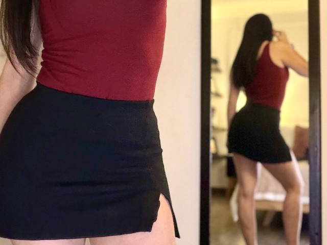 Liliysweet indossa una canotta rossa e una minigonna nera con una fessura laterale, mostrando i suoi fianchi formosi e le gambe toniche in un selfie allo specchio. I suoi lunghi capelli castani sono sciolti..