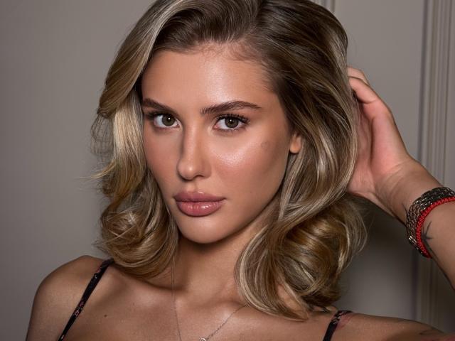 SensualMila ha i capelli biondi e ondulati, gli occhi verdi e le labbra rosa lucide. Indossa una canotta nera con un braccialetto rosso al polso destro, ed è molto sexy..
