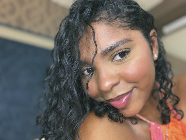 LisaMendez ha i capelli neri e ricci, gli occhi marroni e un sorriso con il rossetto rosa. Indossa una camicetta di pizzo rosa, che mette in risalto il suo carino naso e i suoi piccoli orecchini rotondi..