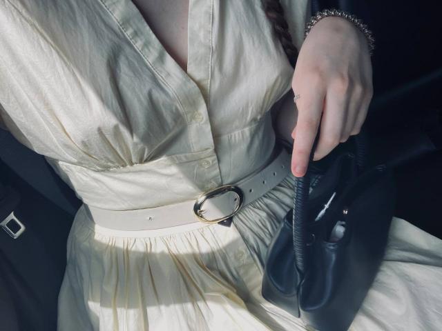 JuttaHillwig's white dress with a silver belt, holding a black leather clutch, her hand with a ring and bracelet, showing her tits in the fabric's soft folds.