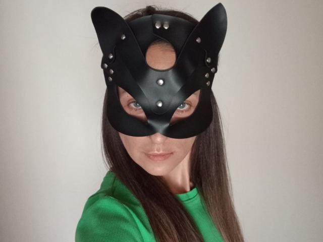 ViktoriiaLu, avec un masque en cuir noir orné d'oreilles de chat qui lui couvre les yeux, portant une chemise verte, et regardant directement la caméra avec un léger sourire..