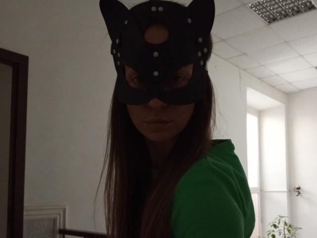 ViktoriiaLu portant un masque de chat noir avec des oreilles, un sweat à capuche vert et de longs cheveux bruns, regardant vers le bas avec une expression sérieuse dans une pièce faiblement éclairée..