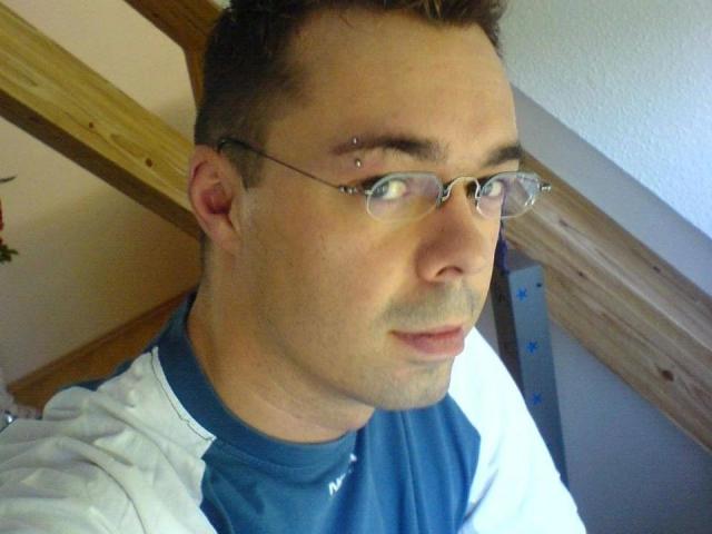 Dannyboy20-fun-hot has glasses, a nose piercing, and a short haircut. He's wearing a blue and white shirt. His face is slightly tilted to the camera.