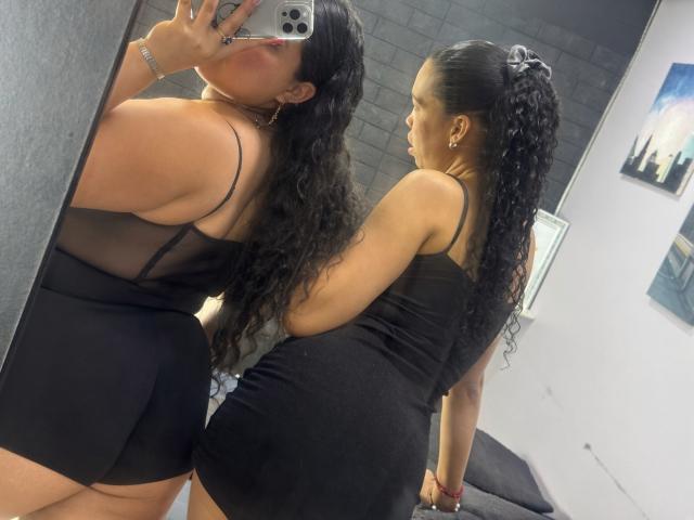 CharlotteTiffany with long curly black hair, wearing a tight black dress, showing her ass in a mirror selfie, holding an iPhone, reflection visible.