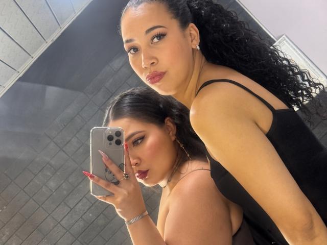 CharlotteTiffany with long black curly hair, wearing a black spaghetti-strap top, taking a selfie in a mirror with her phone, showing off her red lipstick and nails.
