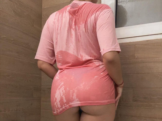 FortuneLisa69 wearing a wet, pink, short-sleeved dress, showing her bare ass, standing in a wooden-tiled shower, with water stains on her back and dress.