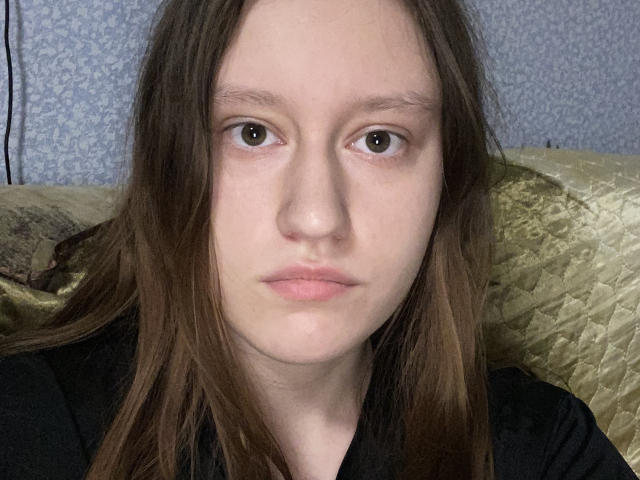 DonetteFiscella has pale skin, brown eyes, and long brown hair. She's wearing a black shirt with a neutral expression, looking straight at the camera.