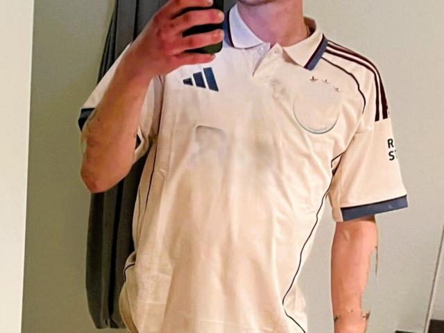Four69 wearing a white German soccer shirt with blue and black stripes, holding a phone, shirt slightly transparent showing a faint outline of their ass. Mirror selfie.