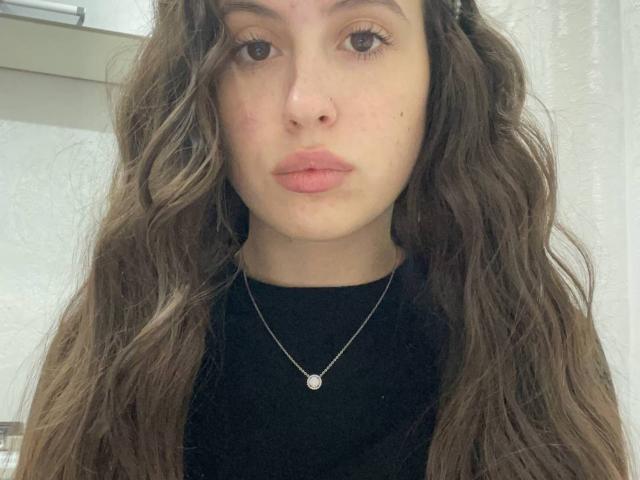 ArnitaFingleton has wavy brown hair, a nose ring, and wears a black top with a silver necklace. Her pink lips are slightly pursed. Her tits are small and cute.