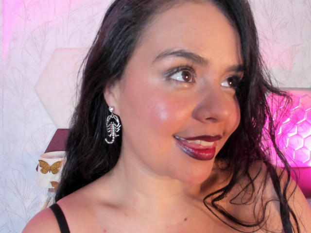 Arielle Wilde heeft lang donker haar, bruine ogen en glanzende, roze-rode lippenstift. Ze draagt zwarte oorbellen in de vorm van een schedel en een zwarte top met spaghettibandjes..