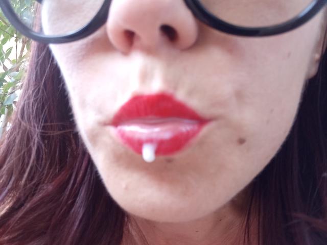 Il viso di OrianaLaFrancaise, con rossetto rosso, una piccola goccia bianca sul labbro inferiore e occhiali con montatura nera, che mostra una pelle leggermente lentigginosa e capelli castano scuro..