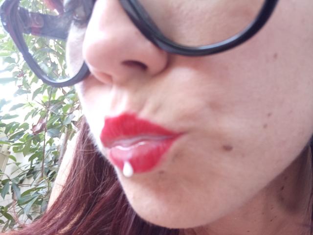 Het gezicht van OrianaLaFrancaise, met rode lippenstift, een kleine witte stip op haar onderlip, en haar neus die iets omhoog staat. Ze draagt een zwarte bril, en haar bruine haar is zichtbaar..