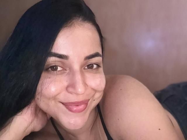 HikariChloe has black hair, brown eyes, and a cute smile with pink lips. She's wearing a black halter top, showing her shoulders and small tits.