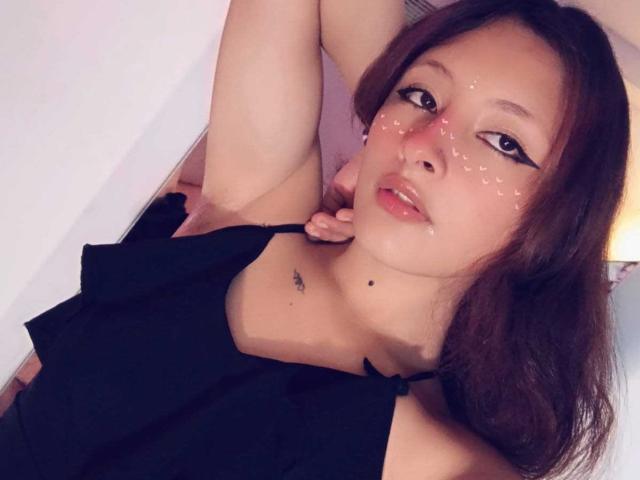 ValentinaRoseX with sparkly glitter on her face, wearing a black halter top, arms raised, brown hair, and a small tattoo under her chin, looking at the camera.
