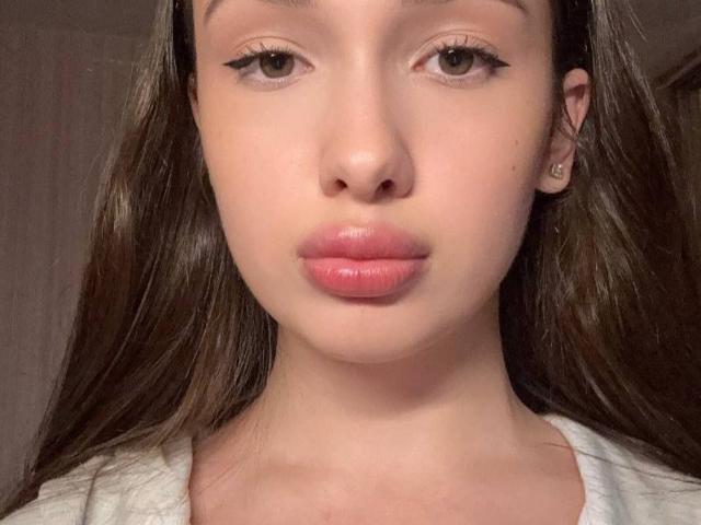 RyanFedorko a un joli visage avec des lèvres roses, des yeux verts et des cheveux bruns. Elle porte une chemise blanche, et ses petites seins sont légèrement visibles. Elle regarde l'appareil photo..