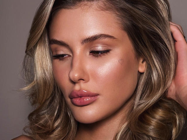 SensualMila's face is gorgeous with shiny, wavy blonde hair, subtle pink lipstick, and closed eyes. She has a smooth, glowing complexion and a relaxed, sensual expression.