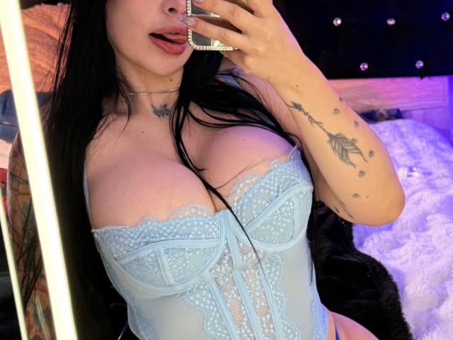 Kkole with large tits, wearing a blue lace corset, black hair, tongue out, holding phone, arm tattoo, choker, mirror selfie.