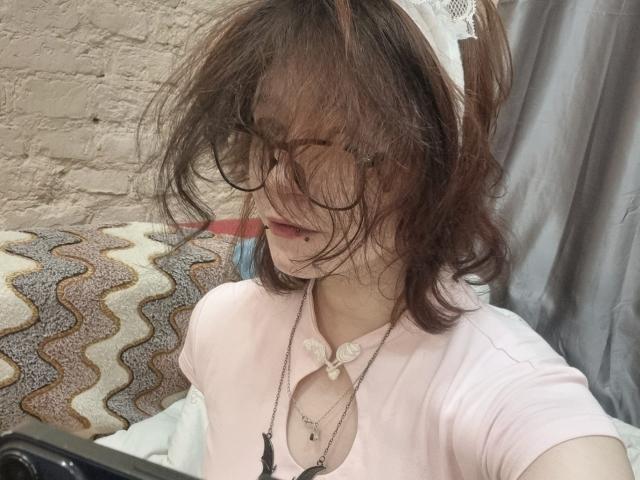 SophiaRenlay has messy brown hair, glasses, and a white lace headband. She's wearing a pink top with a necklace, and her face is partially hidden by her hair.