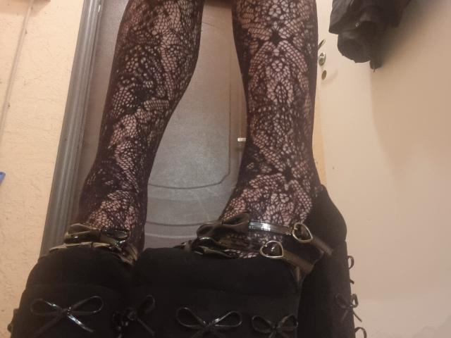 SophiaRenlay's legs in black lace stockings with a floral pattern, wearing black high heels with shiny buckles and lace-up details, standing in a doorway.