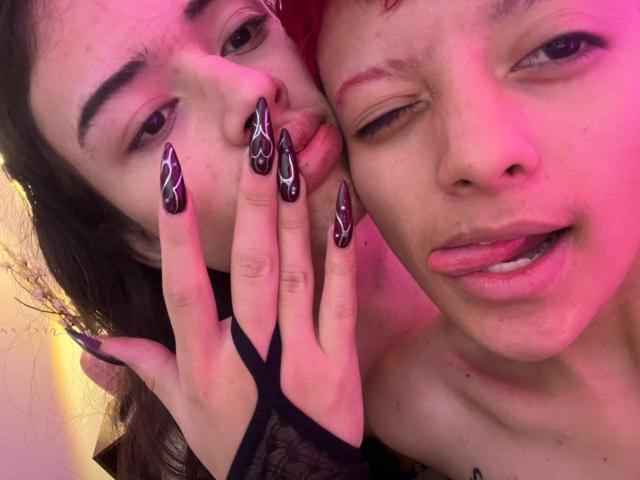 KvsKael with long black nails, pink-tinted face, and red hair, winking, tongue out, hand over face. KvsKael's other hand has black lace fingerless glove.