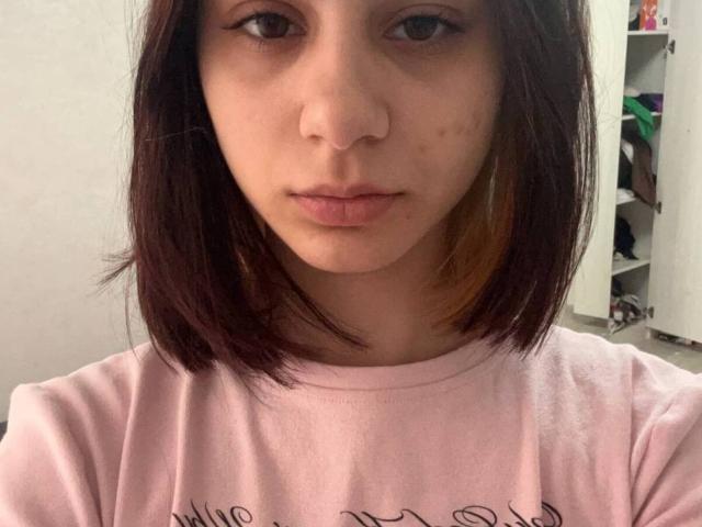 AlixMouton heeft een neuspiercing, bruine ogen en kort donkerbruin haar met een vleugje oranje. Ze draagt een roze shirt en kijkt recht in de camera..