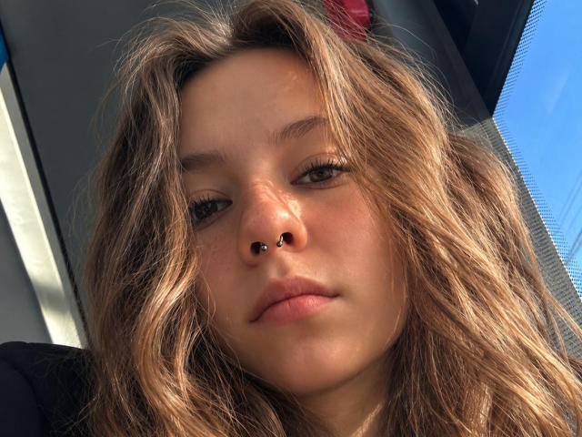 CieraSeidman has wavy brown hair, a nose piercing, and a neutral expression, with sunlight casting shadows on her face. She's in a car, looking slightly to the side.