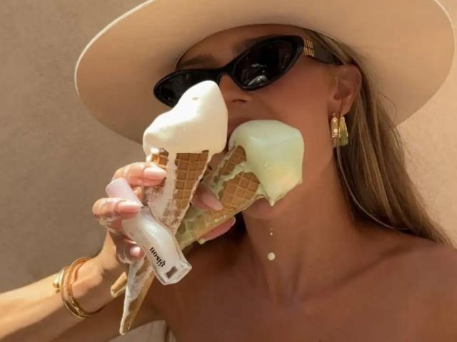 EmillyWalker eating a double scoop ice cream with her tits partially covered, wearing black sunglasses, a white hat, gold earrings, and a bracelet, with a tan skin tone.
