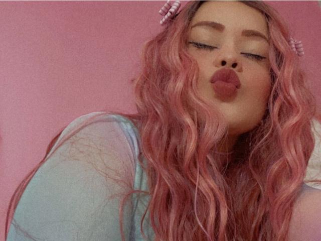 MalloryHearth with pink wavy hair, pouty lips, and blue top, wearing pink hairpins, looking cute and sexy.