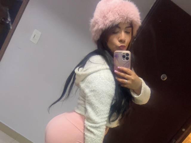 AriLynn, con i suoi lunghi capelli neri, un cappello rosa soffice, una felpa bianca e un sedere formoso, sta scattando un selfie allo specchio, mettendo in mostra il suo sedere prosperoso e i suoi piccoli seni..
