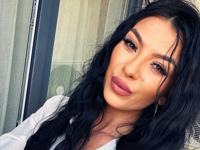 AmelieReea a de longs cheveux noirs ondulés, des yeux marrons, des lèvres pleines roses et une petite tache de beauté sur sa joue droite. Elle porte un haut blanc avec un collier..