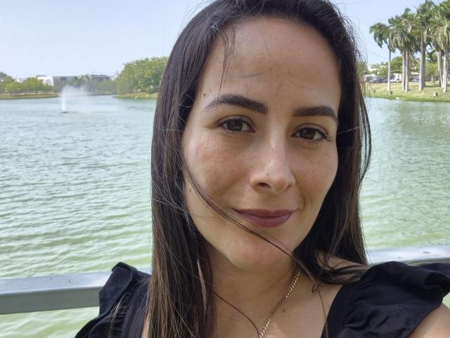 Roussemelinda69 has brown eyes, straight dark brown hair, and a slight smile. She's wearing a black top with puffed shoulders and a gold necklace. Her tits are small.