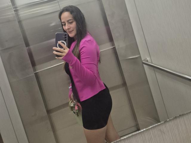 Roussemelinda69 with long black hair, pink jacket, and black shorts, holding a phone in an elevator, showing her ass in a mirror selfie.