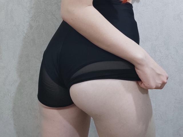 SheritaChieng's pale skin and black sheer butt shorts, showing her ass and thighs. She's pulling the shorts up with her right hand, her red hair slightly visible.