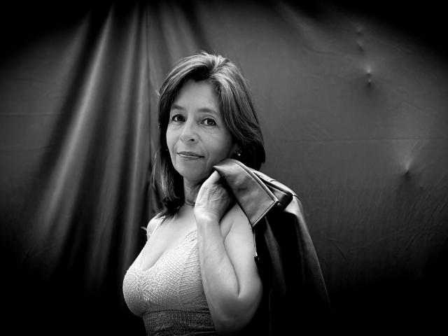 Black-and-white photo of SabinaDeluxe with medium tits, wearing a lace top, holding a jacket on her shoulder, smiling slightly, with medium-length dark hair.