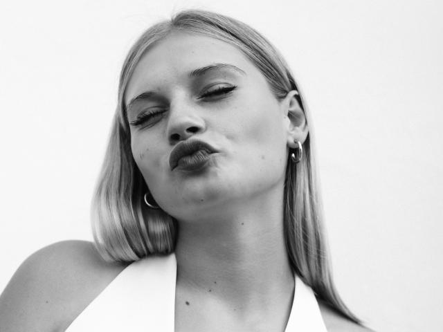 Black-and-white photo of EdyTheViard with pouty lips, long blonde hair, hoop earrings, and a white top. Her eyes are half-closed and she's slightly leaning to the side.