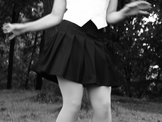 EdyTheViard's black pleated skirt, white vest, and bare legs, with arms slightly raised, in a black-and-white photo. EdyTheViard's ass is covered by the skirt.