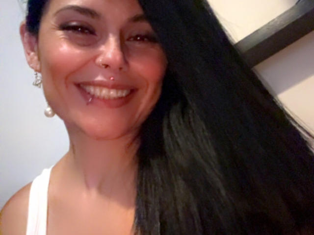 CharlotteCrofort with long black hair, smiling with bloody lip, white tank top, nose ring, and pearl earrings, showing off her tits slightly. She's got a cute, sexy look.
