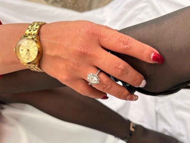 StangelarRivera's hand with red nails, gold watch, and diamond ring, resting on her black panty-clad pussy, wearing sheer black stockings.