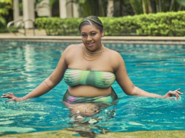 BiancaForest in a pool, wearing a green and blue striped strapless top, her hands in the water, showing her curvy ass and large tits, with a gold necklace.