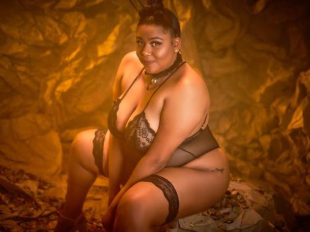 BiancaForest with curvy, large tits and thick ass, wearing sheer black lingerie and lace stockings, sitting on a rock, smiling, with brown hair in buns, warm lighting.