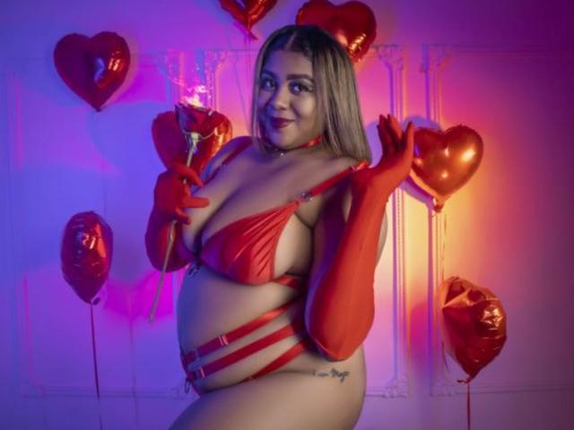BiancaForest with large boobs, chubby ass, and a pregnant belly, wearing red strappy lingerie and gloves, holding heart balloons, smiling, under purple and pink lights.