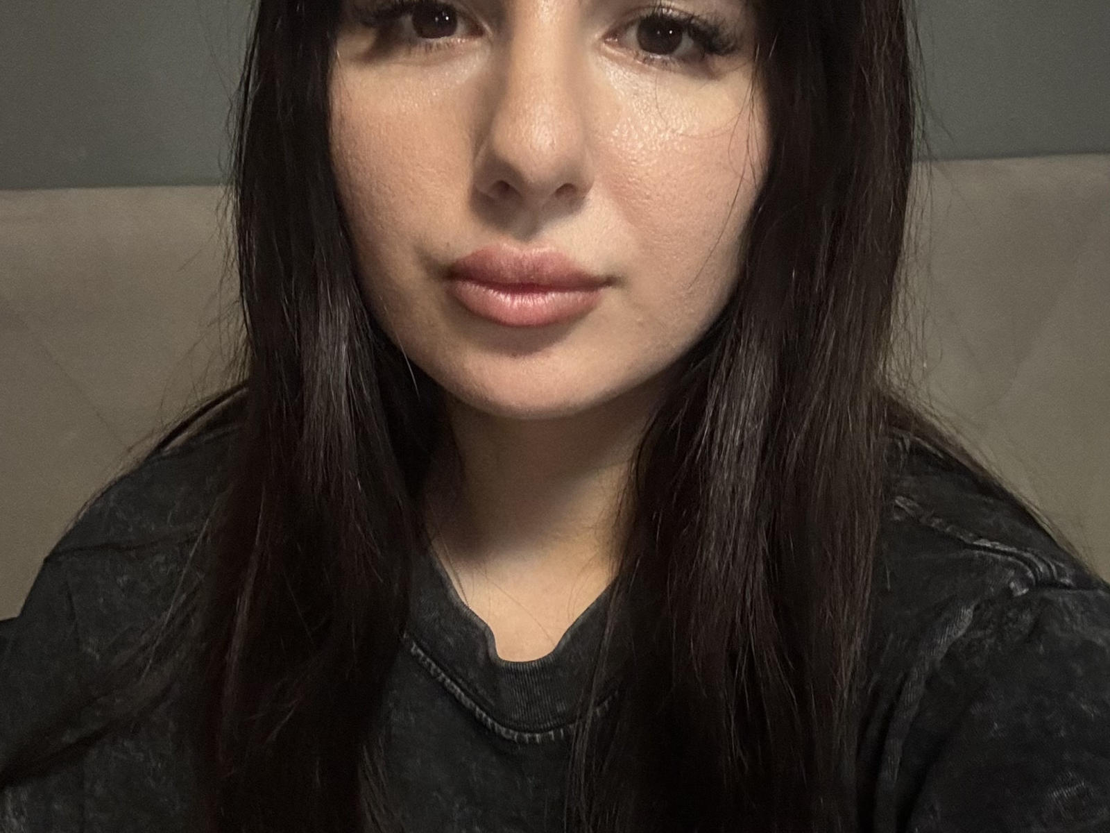 Le visage de Carmina Stancle, avec ses longs cheveux bruns foncés, sa peau claire et son maquillage discret, porte une chemise noire. Elle a des lèvres pleines et roses, et une expression neutre, légèrement curieuse..