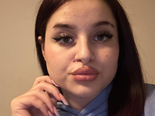 Luucie has full lips, long dark brown hair, and thick black eyelashes. She's sucking her finger with her pink-manicured hand, looking at the camera with a slightly pouty expression.