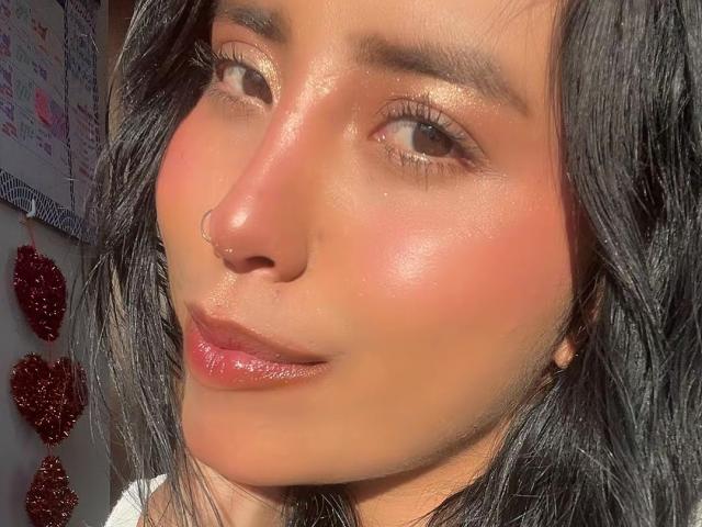 ElizabethMacy's shiny face with glowing, sparkly brown eyes and pinkish blush. She has black, wavy hair and glossy, slightly parted pink lips. Sunlight highlights her smooth, shiny skin.