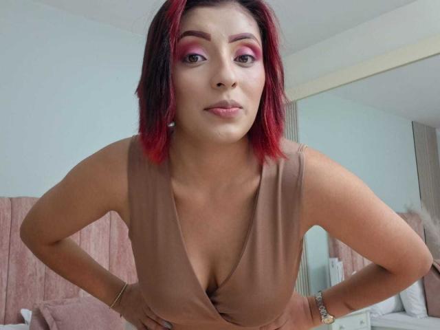 LizBonnet with red-tipped hair, pink eyeshadow, brown dress, hands on hips, showing her tits, subtle smile, bedroom setting, mirror reflection, bracelet, light skin, confident.