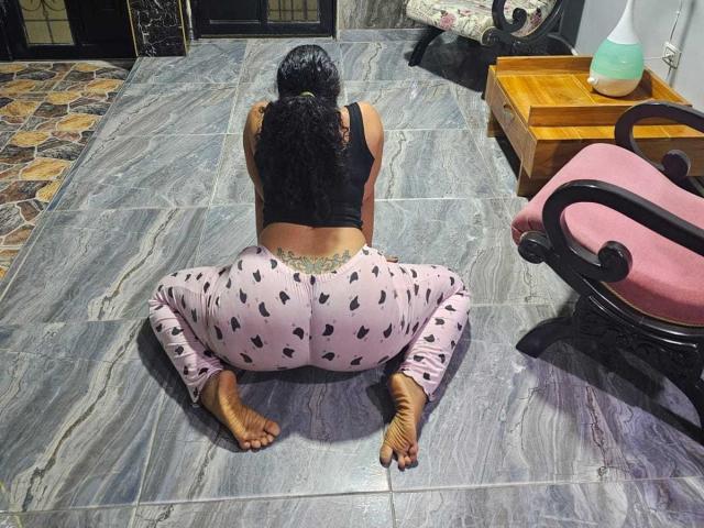 NaomyHott69, butt up, squatting on gray tile floor, wearing pink heart-patterned leggings, black tank top, and no shoes, with a tattoo on her lower back.